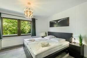 A modern bedroom with a large bed, a nightstand, a wall-mounted artwork, and a view through a window. - Holiday Home 'Büffel' with Private Terrace and Wi-Fi (Niedenstein)