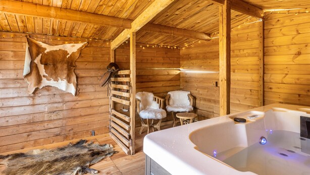 L’intérieur d’un chalet en bois, avec un jacuzzi, des tapis en fourrure et un plafond en bois.