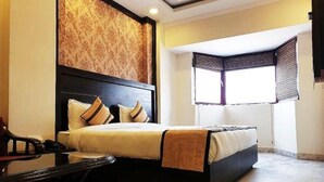 A bedroom with a bed, a desk, and a window with blinds.
