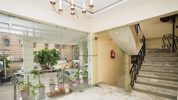 A modern hotel lobby with a glass railing, potted plants, a staircase, and a fire extinguisher.