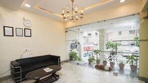 A reception area with a black sofa, a small table, a chandelier, a clock, framed certificates, and a glass door with potted plants.
