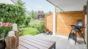 A patio with a wooden table, a barbecue grill, and a view of a garden. - FENJOY vacation apartment No°9 with terrace | garden | BBQ (Bernau am Chiemsee)