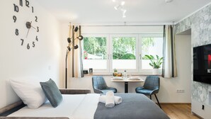 Una camera d'albergo con un letto, una sveglia, una TV e una finestra che si affaccia sul verde.