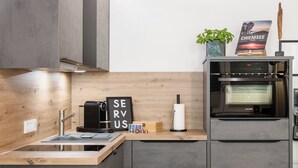 Una cucina moderna con forno integrato, macchina del caffè e un cartello con su scritto "SERVE US".