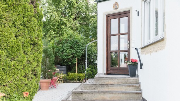 Un edificio bianco con una porta marrone, scale che conducono a un portico e piante in vaso.