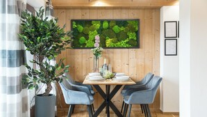 Een eethoek met een houten tafel, vier stoelen, een potplant en een wanddecoratie van groen mos.
