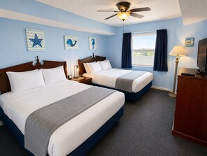A hotel room with two beds, a ceiling fan, a window with curtains, and artwork on the walls.