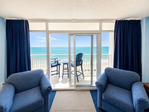 Ein Balkon mit zwei Sesseln, einem Tisch und Stühlen mit Blick auf einen Strand.