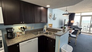 A compact kitchen with dark cabinets, a dishwasher, a coffee maker, and a sink. - Atlantic Lux. Spacious relax. (Myrtle Beach)