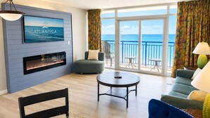 Una sala de estar con chimenea, televisor, sofá, sillón y un balcón con vista al océano.