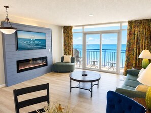 Una sala de estar con chimenea, televisor, sofá, sillón y un balcón con vista al océano.