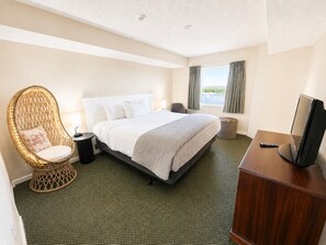 A hotel room with a bed, a television, a wicker chair, and a view of the outdoors.