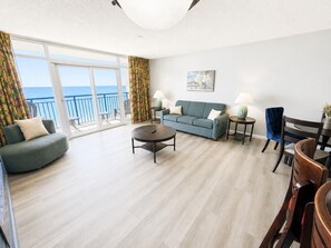 A spacious living room with a balcony, a sofa, a coffee table, and a dining area with chairs and a table.