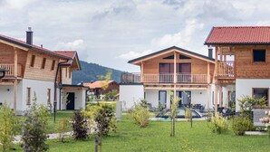 A row of wooden houses with balconies, a swimming pool, and a mountainous backdrop.