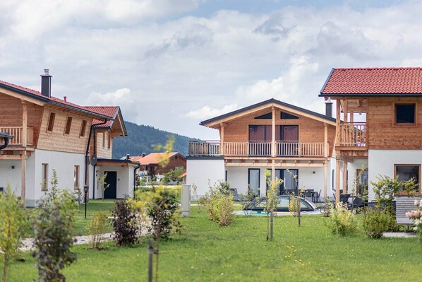 A row of wooden houses with balconies, a swimming pool, and a mountainous backdrop.