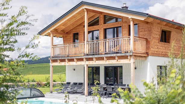 A wooden cabin with a balcony, a pool, and a view of a green landscape.