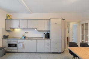 A compact kitchen with a stove, oven, sink, and a dining area with a table and chairs.