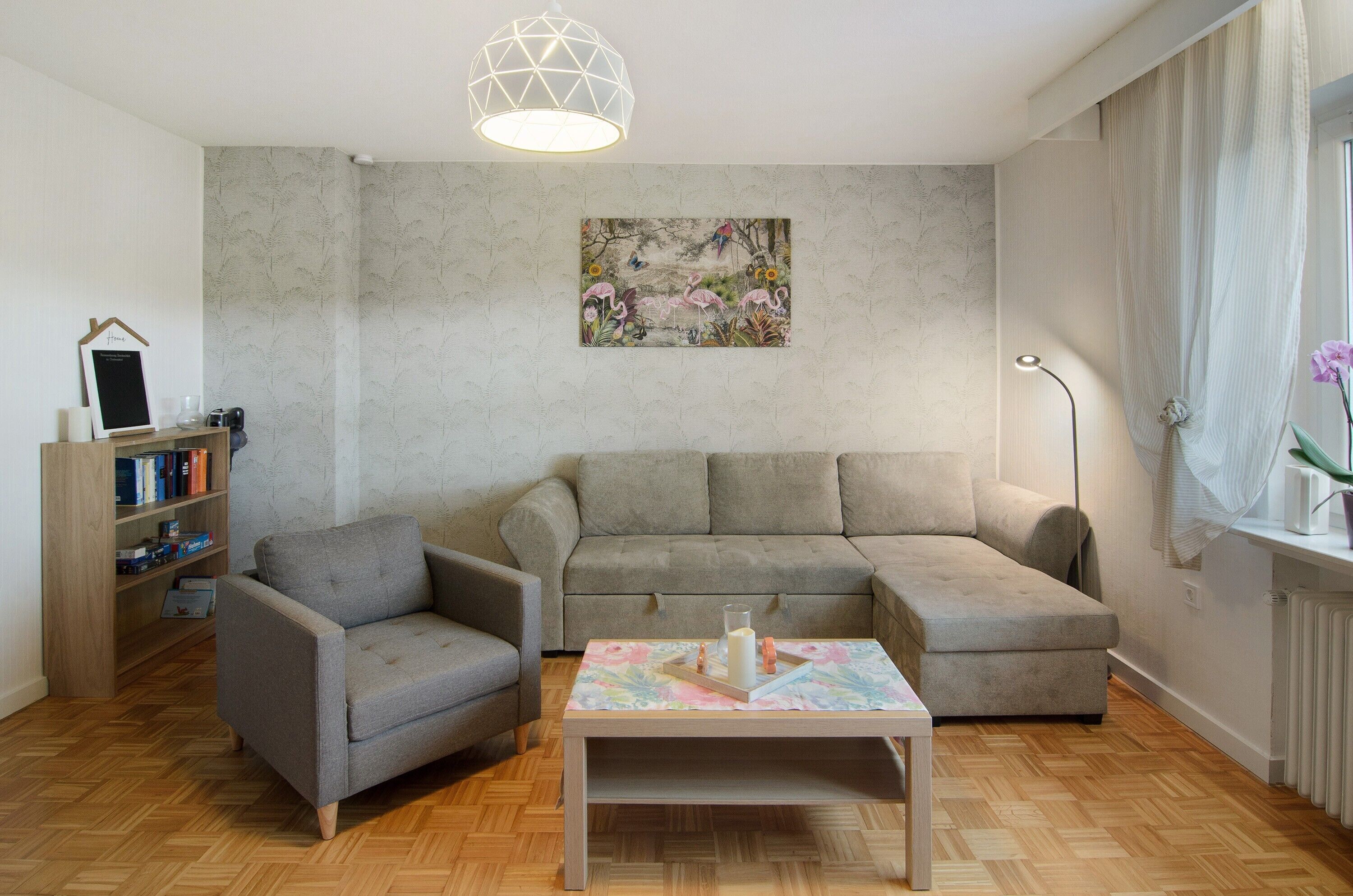 A living room with a sofa, armchair, coffee table, bookshelf, and a painting on the wall.