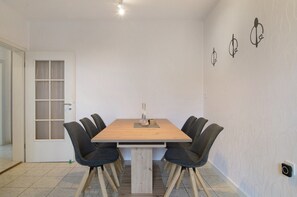 A dining area with a wooden table, six chairs, a door with frosted glass panels, and wall-mounted light fixtures.