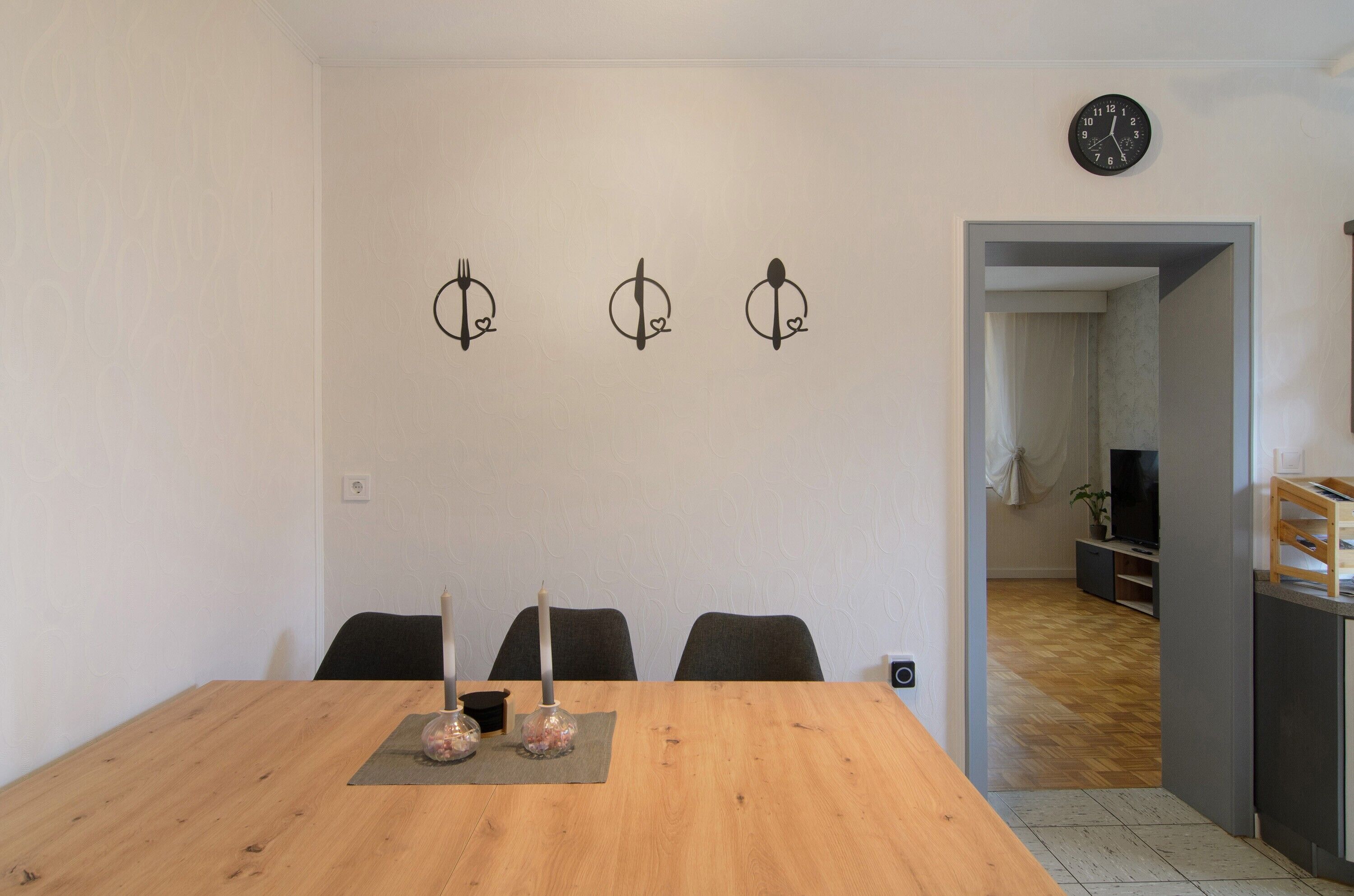 Un comedor con una mesa de madera, tres sillas, un candelabro y lámparas fijadas a la pared.