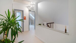 Un pasillo con una planta, un cartel que indica el baño, una escalera y un estante con una botella.
