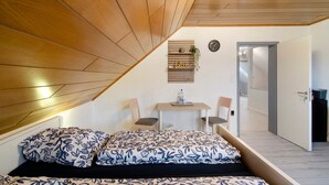 Un dormitorio con cama, escritorio, dos sillas, un reloj de pared y una puerta que da a otra habitación.