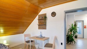 Una habitación con techo inclinado, una mesa de madera con sillas, un reloj de pared y una planta en maceta.