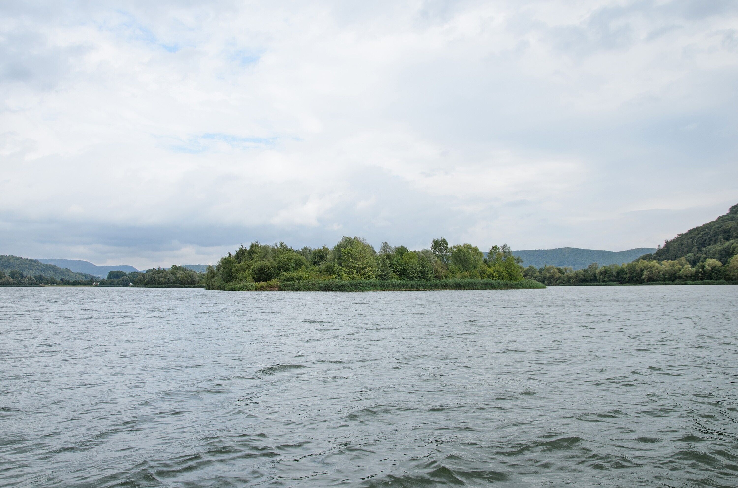 A calm lake with a small island in the center, surrounded by hills.