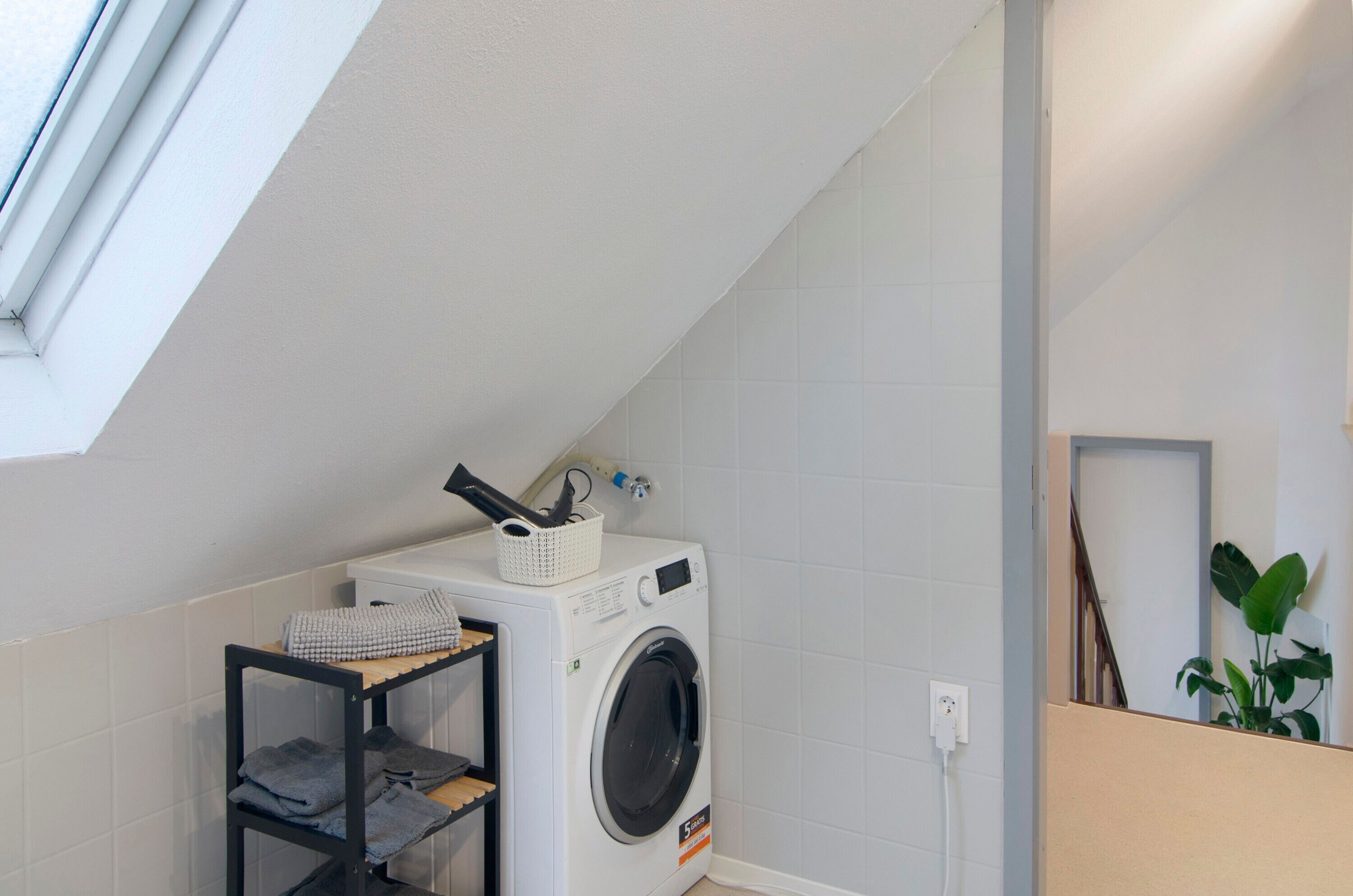 A laundry area with a washing machine, a shelf with folded towels, and a plant.