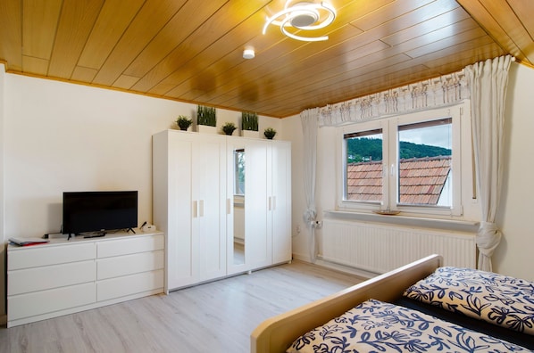 Une chambre à coucher avec un lit, un téléviseur posé sur une commode, une armoire et une fenêtre donnant sur un immeuble.