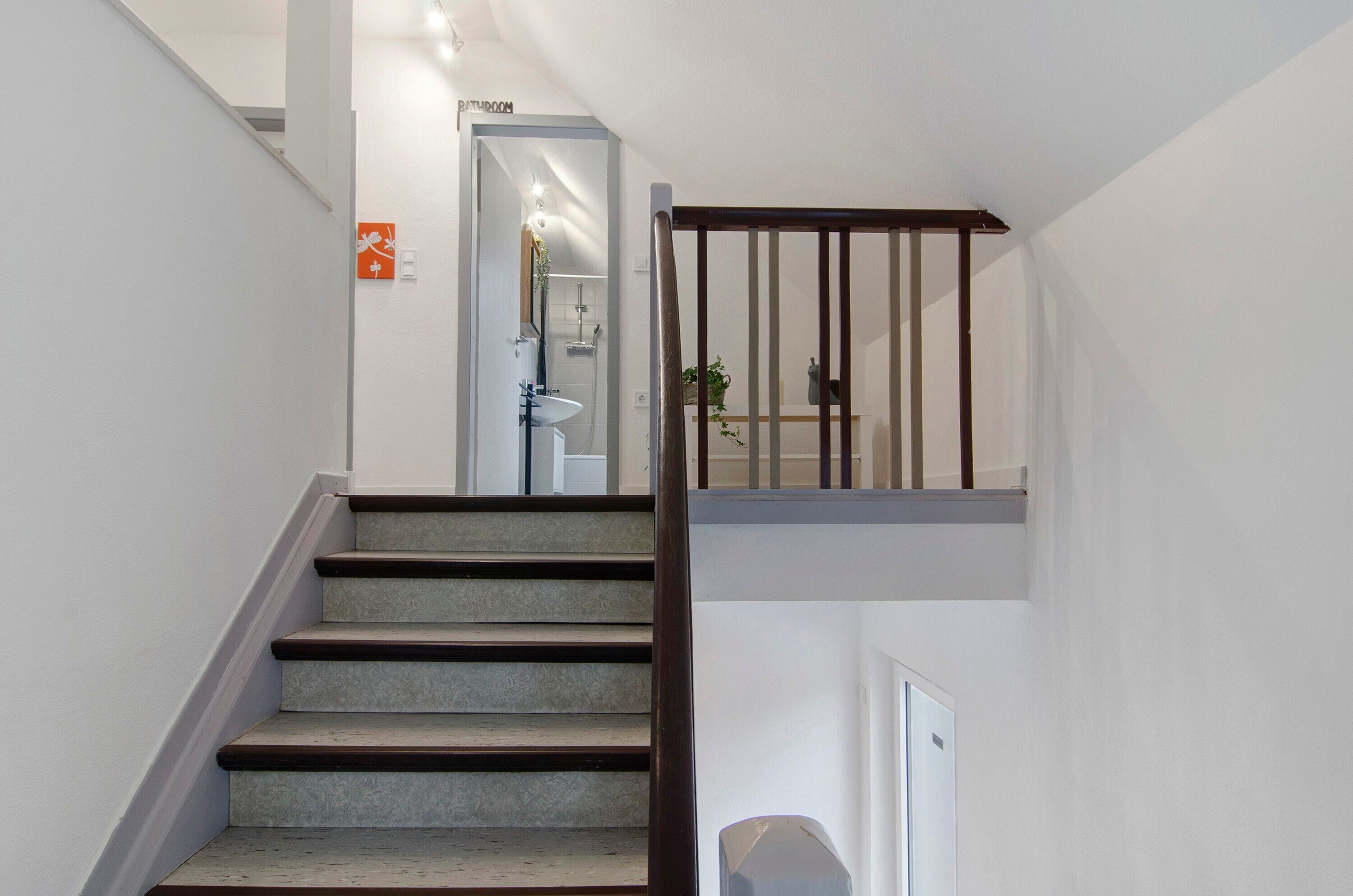 A staircase with a wooden handrail leading to a bathroom with a toilet and sink.