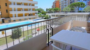Un balcon d’hôtel avec une piscine, des meubles blancs et une vue sur d’autres immeubles.