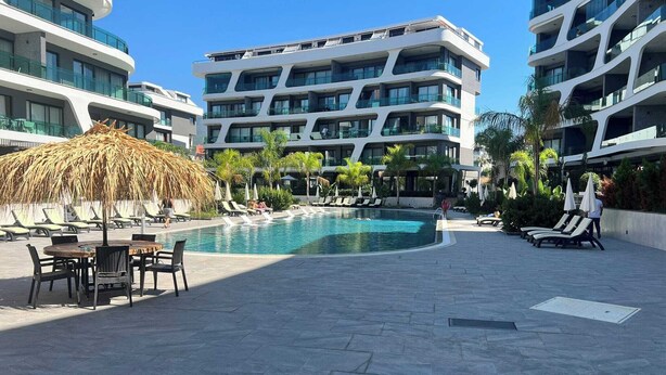 A modern hotel with a central swimming pool, lounge chairs, and a thatched umbrella. - Modern Comfort in Oba: New 1+1 Apartment in Sol Garden (Alanya)