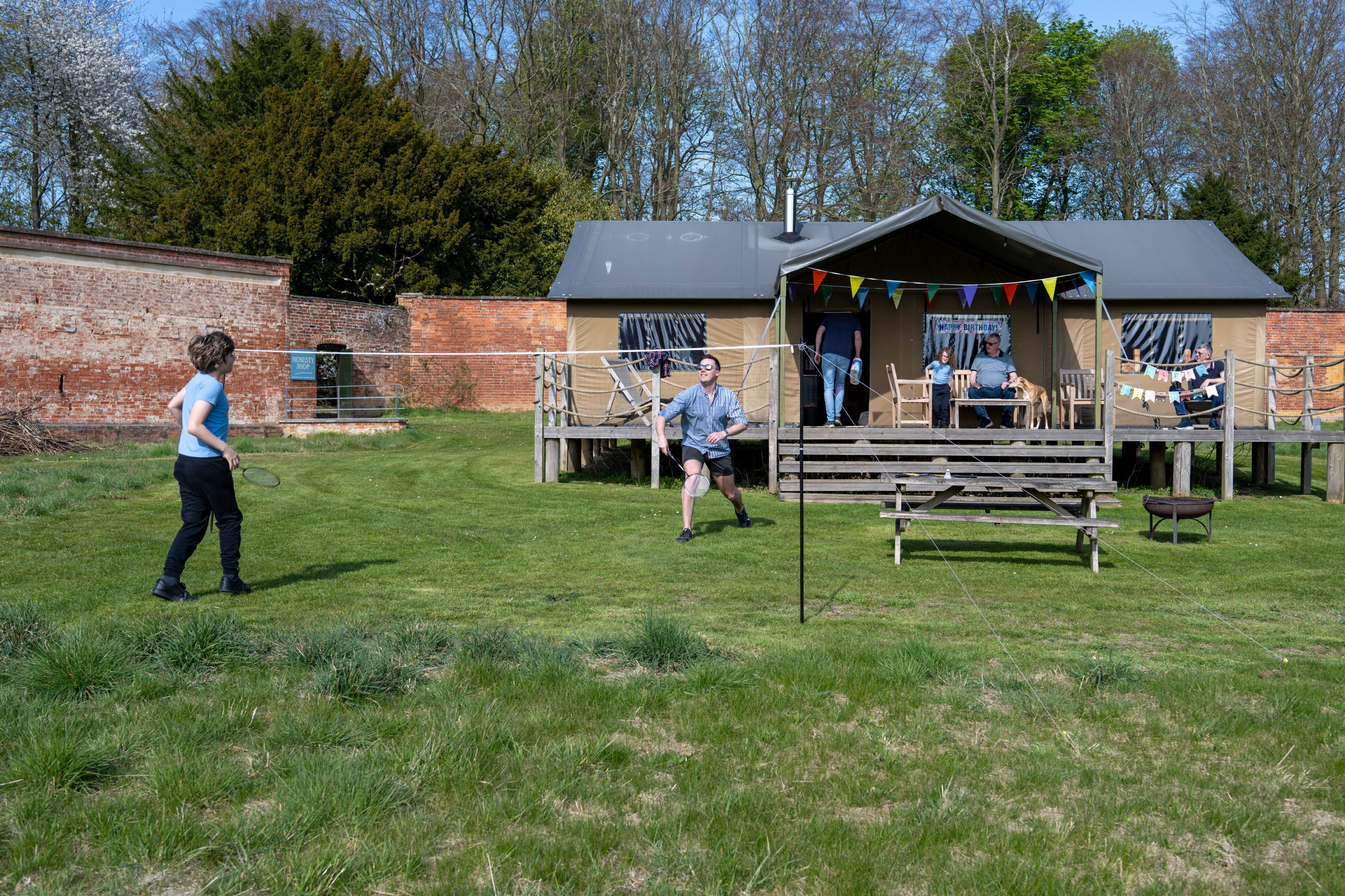 Ein grünes Areal im Freien mit einem kleinen Gebäude, möglicherweise ein Pavillon, mit Dach und überdachter Sitzgelegenheit.