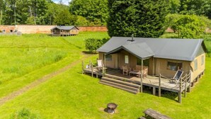 Un chalet doté d’une terrasse et de meubles de jardin, entouré d’une végétation luxuriante et surplombant un ciel dégagé.