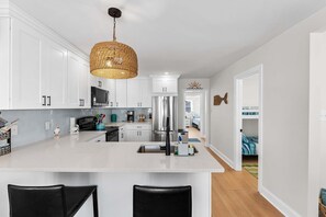 A modern kitchen with white cabinetry, a central island with bar stools, a stainless steel refrigerator, and a woven pendant light.