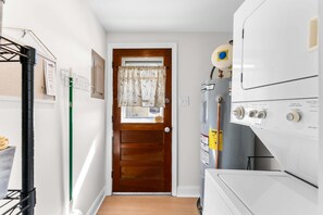 Ein Waschraum mit gestapelten Waschmaschinen und Trocknern, einer Holztür mit Fenster und einem an der Wand befestigten Regal mit Reinigungsmitteln.
