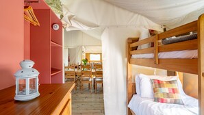A cozy room with bunk beds, a wooden table with a lantern, and a dining area with chairs and a table. - Dog friendly Safari Tent, Swallow at Sweffling Hall, Suffolk (Saxmundham)