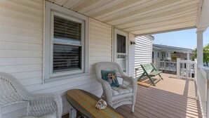 A covered porch with wicker chairs, a bench, and a window with blinds.