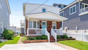 A two-story residential building with a front porch, brick foundation, and a white fence.