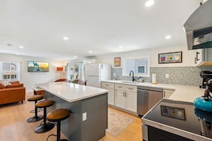 A modern kitchen with a central island, bar stools, a coffee machine, and a dining area with a sofa and chairs.