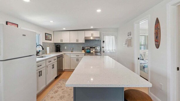 A modern kitchen with white cabinets, a central island, and a view into the adjacent bedroom.