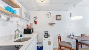 A compact kitchen with a sink, microwave, and coffee maker, a small refrigerator, a dining table with chairs, and a wall-mounted clock. - Top-Floor Studio with a Heated Pool & Parking (Wildwood)