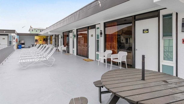 A row of rooms with large windows, a covered outdoor seating area with tables and chairs, and a mural on the wall. - Top-Floor Studio with a Heated Pool & Parking (Wildwood)