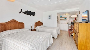 A room with two beds, a wooden headboard, a whale decoration, a television, and a kitchenette. - Top-Floor Studio with a Heated Pool & Parking (Wildwood)