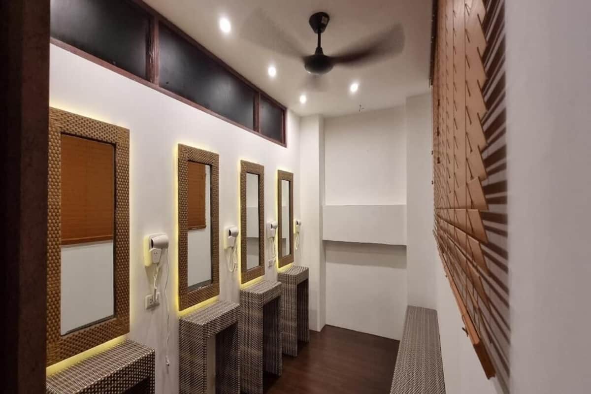 A row of three bathroom stalls with individual mirrors and a ceiling fan.