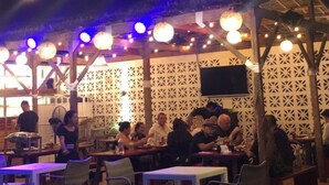 Ulkoterassi, jossa on pöytiä ja tuoleja, valoketjuja ja puinen pergola.