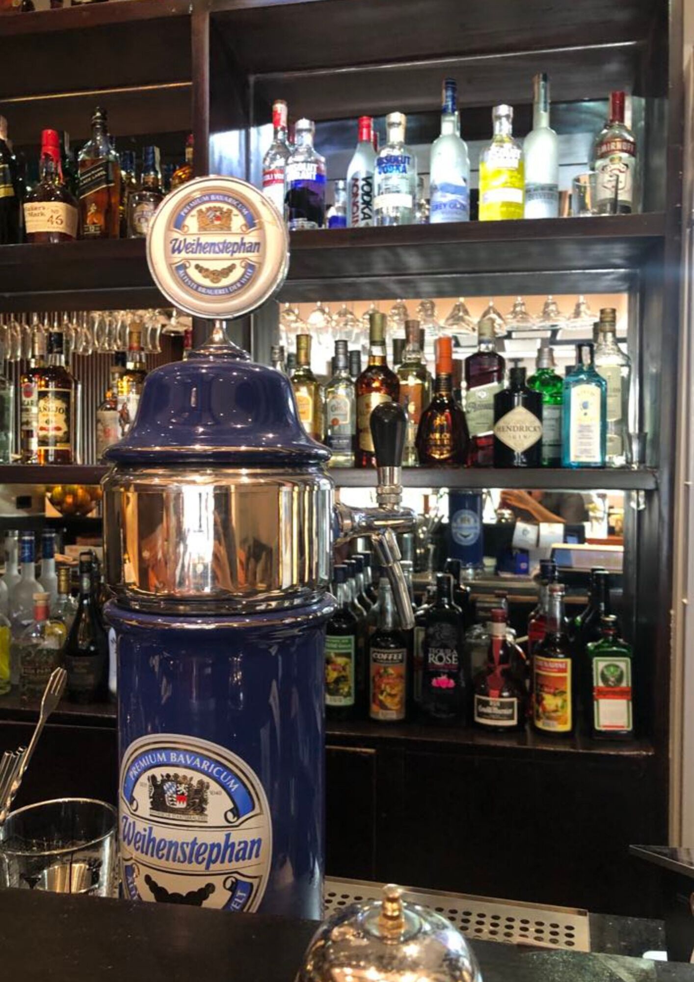 Uma área de bar com uma torneira de cerveja Weihenstephan e diversos frascos de bebidas alcoólicas.