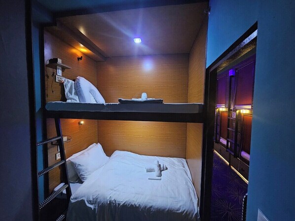 Quarto com beliche, cabeceira de madeira, pequena prateleira e janela com cortinas.