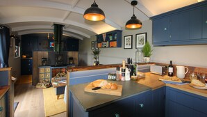 A modern kitchen with blue cabinets, a central island with bread, a toaster, and a wine bottle. - Top Farm Shepherds Lodge, nestled in a peaceful farm in Marsham, North Norfolk (Marsham)